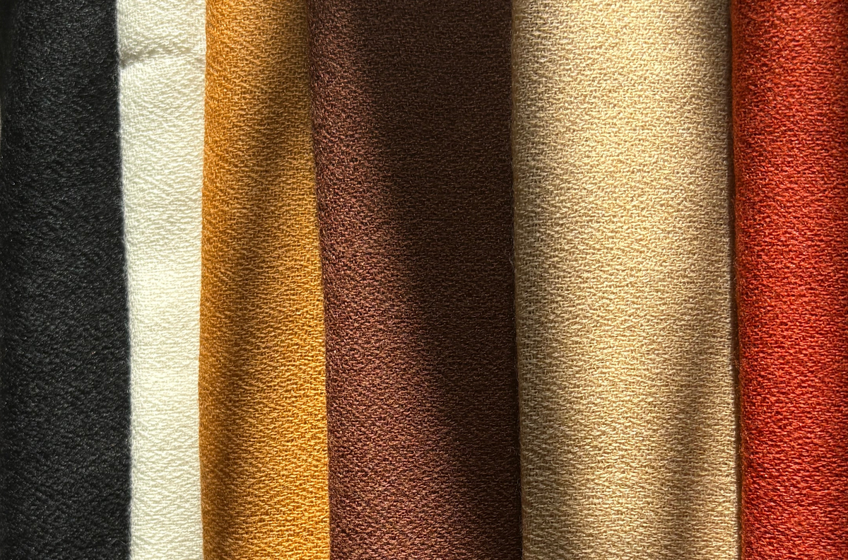 Six vertical fabric swatches in black, off-white, mustard yellow, dark brown, beige, and rust red, each with a subtle woven geometric texture.
