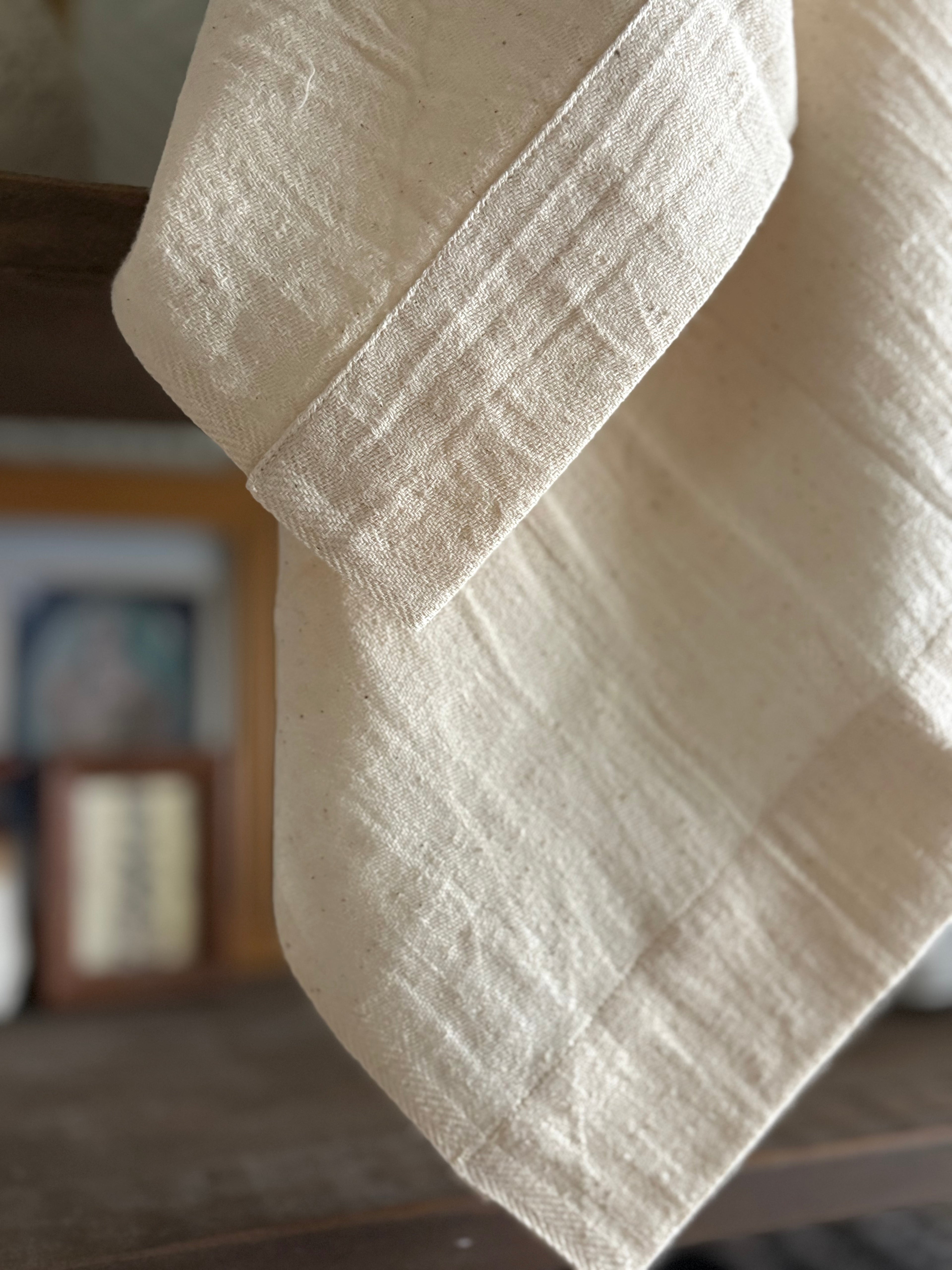 A close-up of a light cream or off-white linen fabric draped over a dark wooden surface, showing its natural textured weave.