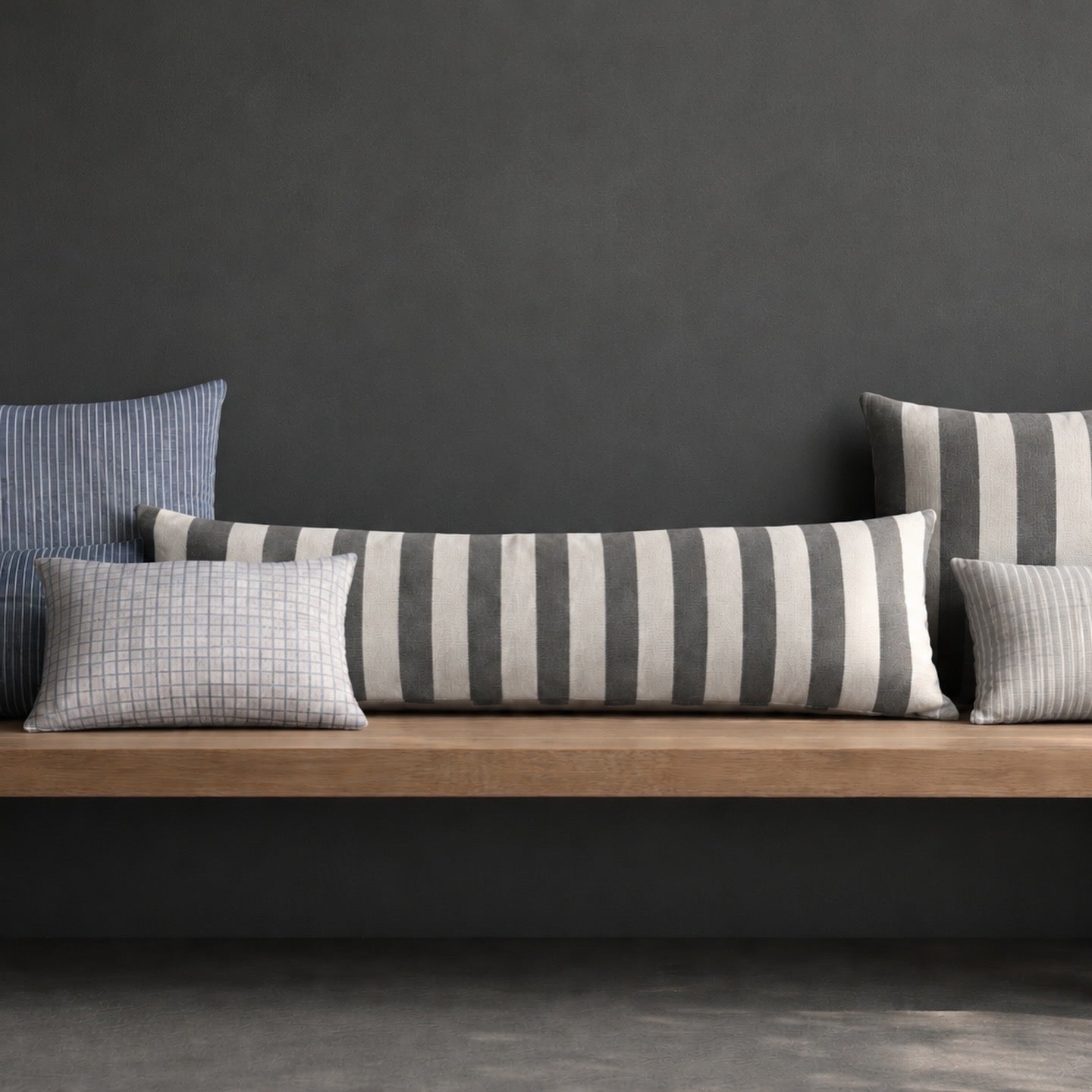 Set of striped and checkered cushions on a wooden surface against a dark gray wall.