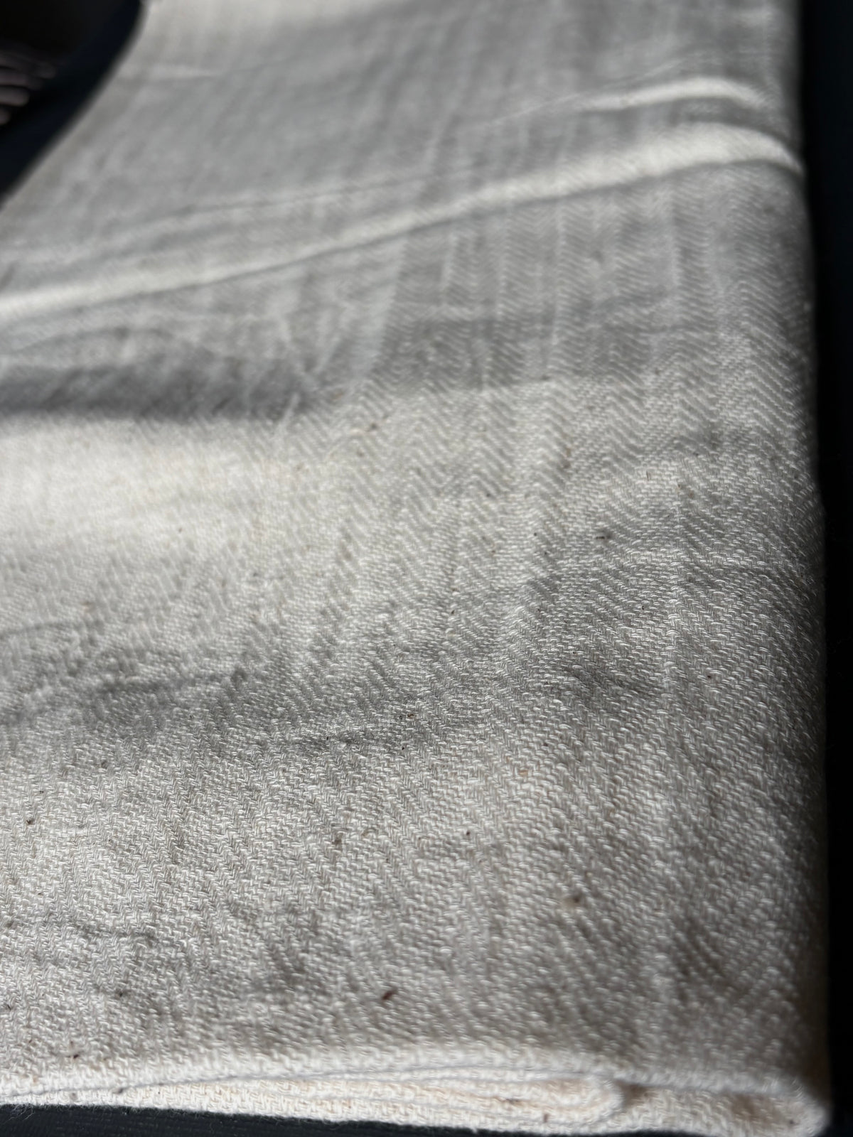 A close-up of a folded ivory linen fabric with a visible herringbone weave pattern. handwoven twill. kala cotton.