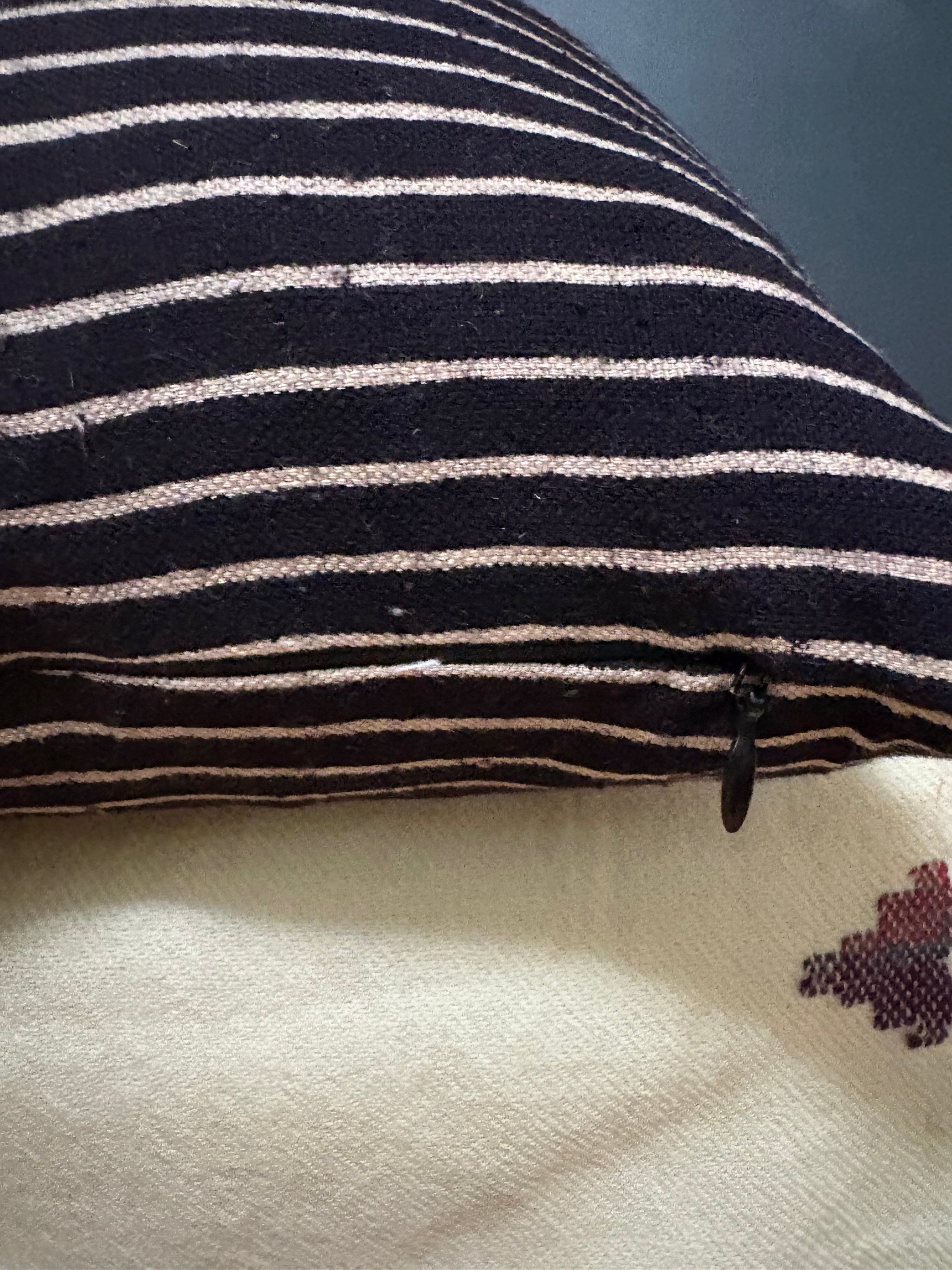 A close-up of a striped woven cushion cover with horizontal black and off-white stripes, showing a small black zipper pull and part of the fabric texture.