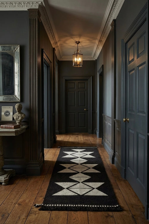 Long hallway with dark walls, wooden floor, and a black and white patterned rug.