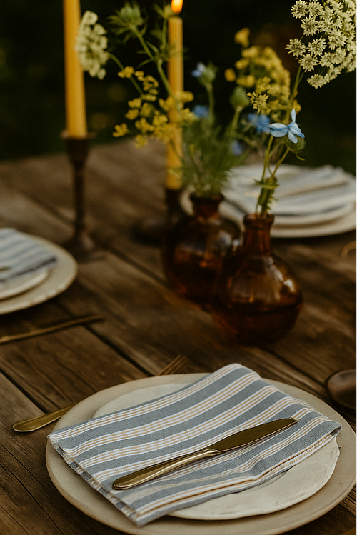 Dining table set with plates, napkins, candles, and flowers outdoors.
