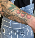 Person wearing a blue apron with a tattooed arm visible