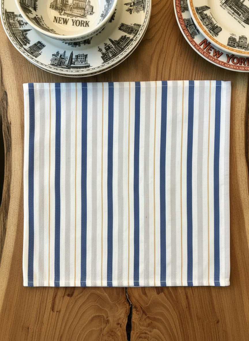 Striped cloth napkin on a wooden surface with decorative plates in the background.