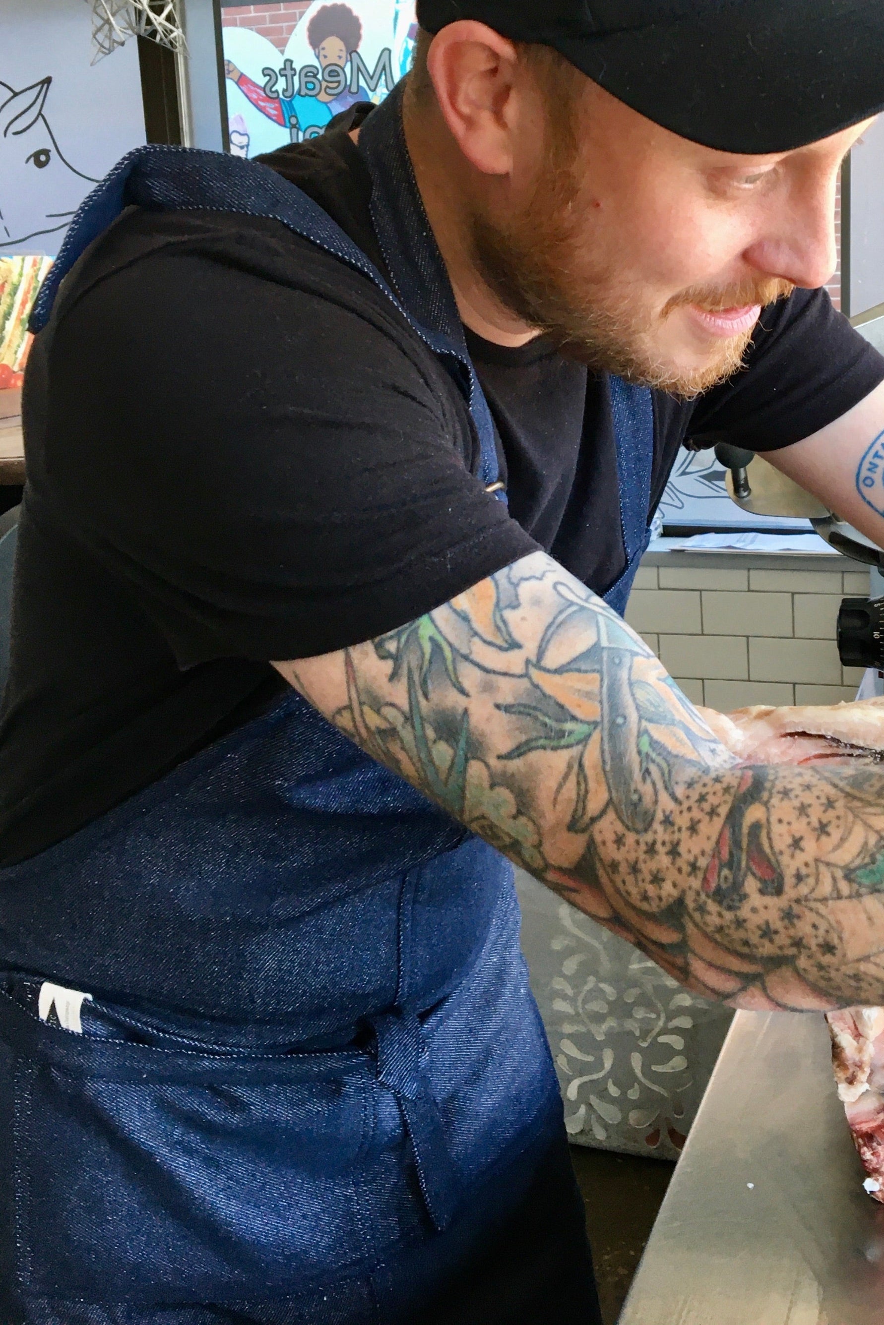 Man with tattoos wearing a recycled cotton denim apron working in a kitchen setting